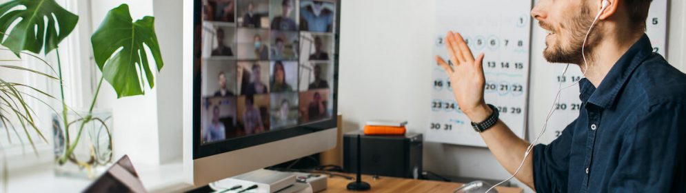 Jeune homme participant à un appel vidéo Zoom sur un ordinateur depuis son bureau personnel, dans le cadre du confinement et du télétravail mis en place pendant la pandémie de Covid-19.